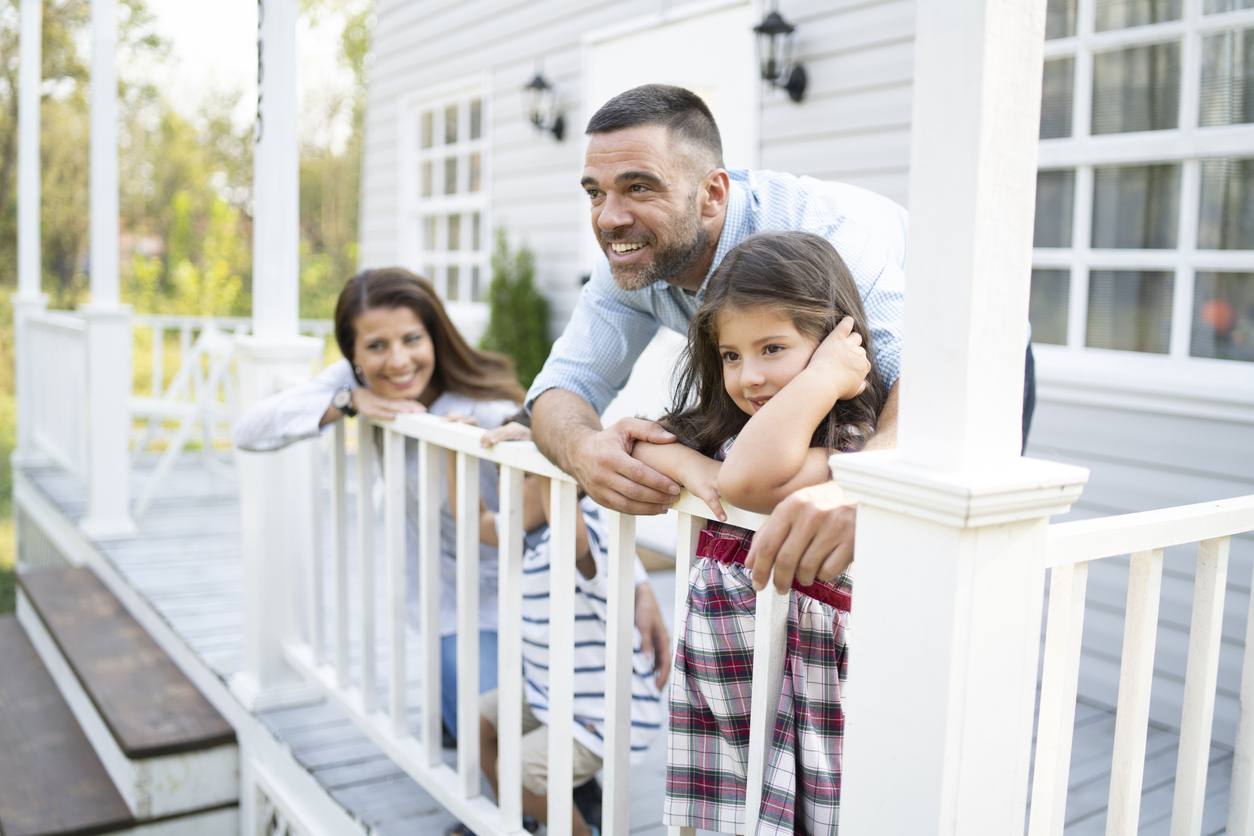 Family with two children leaning on fence in front of their home